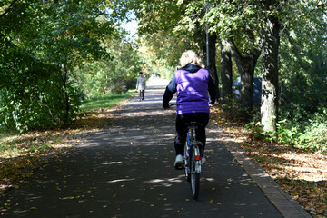 Beginning of autumn. Sunny day. A cyclist is riding along a bike path in a park area, and a pedestrian is walking towards him. bokeh