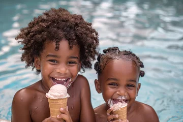 Poster Dos niños juntos dentro del agua en la piscina sonriendo y comiendo un helado. Niños afroamericanos sonriendo dentro de la piscina. © BONI