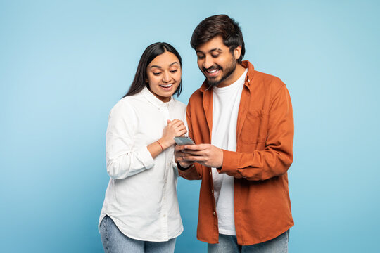 Fototapeta Excited indian couple looking at mobile phone using application, studio