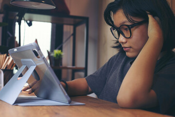 Asian children using digital tablet with stylus pen write and do homework at home. Thai Student wear glasses working online and use headphone to study for the exam. Education and E-learning concept.