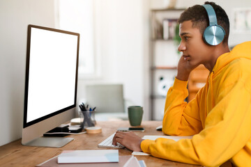 Pensive teen guy at desk with headphones and computer