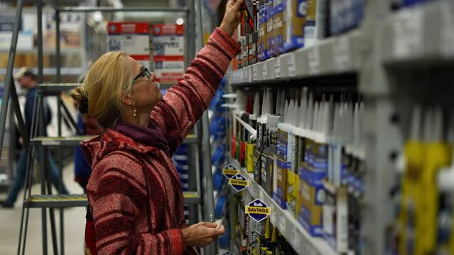 Mature woman shopping in hardware store looking for home improvement products. Concept of home remodeling shopping experience.