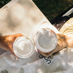 two people's hands holding coffee in the sun