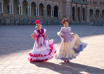 Two beautiful little girls dancing flamenco dressed in typical gypsy costume holding their dress...