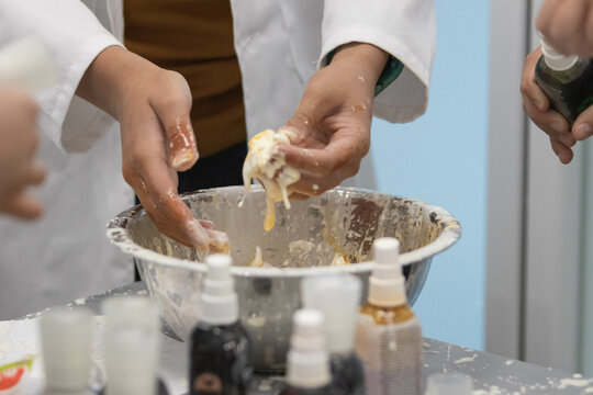 Child plays with food attempting a science experiment with adult supervision while wearing a scientific gown. Close up shot of hands