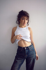 sexy fashionable young curly-haired woman in jeans and white T-shirt standing against the white wall of the house.