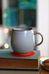 Cup of tea or coffee, pile of books, plate of cookies, reading glasses, e-reader and pen on the table. Colorful rainbow bookshelf in the background. Selective focus.