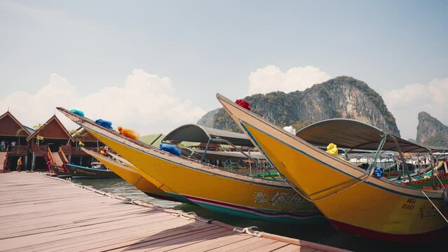 Boats are moored in the sea in the harbour. Colorful thai boats moored by the rocky shore in the blue sea during holiday time. Tourist attraction with pier, seaside, enjoy travel, adventure concept.