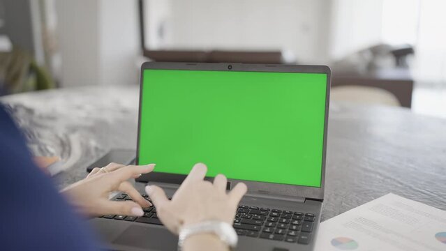 Dona types on laptop with green screen