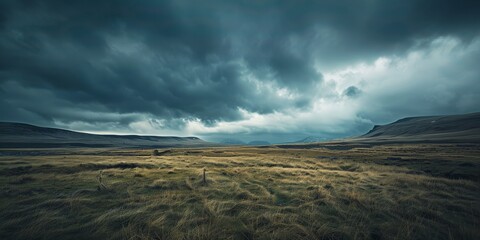 A field of grass with mountains under a dramatic grey sky in the background - Powered by Adobe