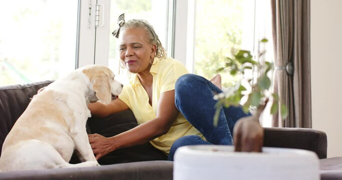 An African American senior woman is sharing a moment with her dog on a sofa at home
