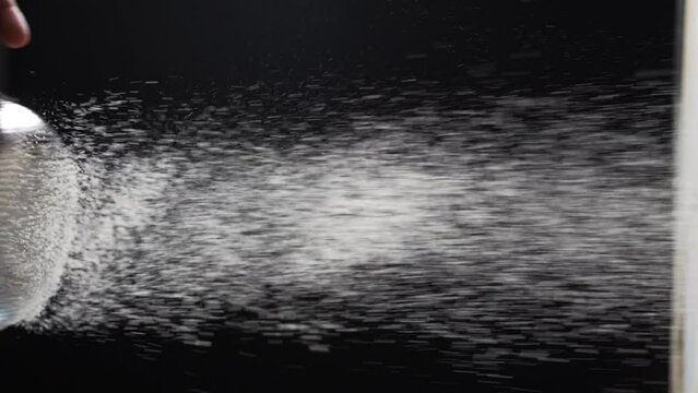 Sifting white flour through a sieve against black background