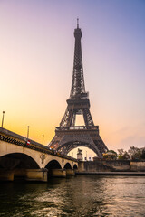 Fototapeta na wymiar A captivating view of the Eiffel Tower and a bridge over the Seine River at sunrise. The sky is painted with warm hues, casting a serene atmosphere over Paris, France.