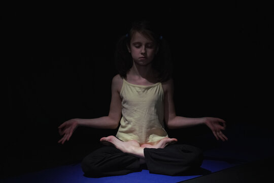Young yogi girl practicing yoga lesson, breathing, meditation, doing Ardha Padmasana exercise, Half Lotus pose with mudra gesture, working out. Horizontal image.