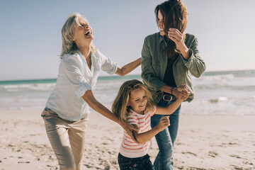 Happy family with grandmother, mother, and daughter playing on the beach