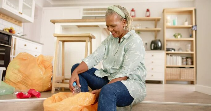 A senior African American woman sorts recycling items on her kitchen floor