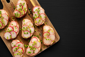 Homemade Lemon Radish Tartine on a wooden board on a black background, top view. Copy space.