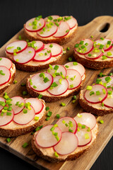 Homemade Lemon Radish Tartine on a wooden board on a black background, side view.