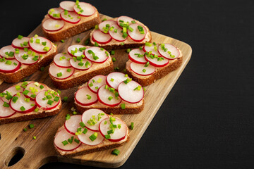 Homemade Lemon Radish Tartine on a wooden board on a black background, side view.