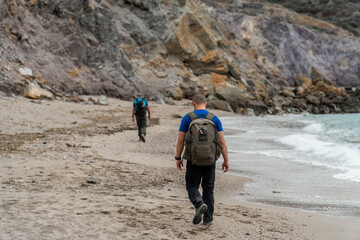 Hikers walking along a wild and lonely beach, near cliffs. 