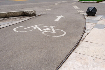 A white bicycle symbol with an arrow, indicating a designated bike lane on a curved city street.