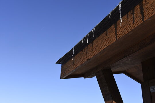 An image of melting icicles hanging from an outdoor wooden structure under a dark blue Winter sky
