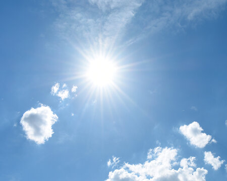 An outdoor image of a blue sky, puffy white clouds, and a bright sun