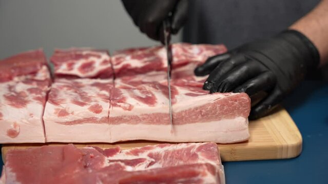 A man in black gloves cuts pork meat on a cutting board. Pork cooking demonstration.