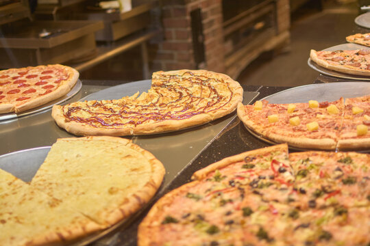 Image showing a selection of gourmet pizzas with different ingredients, with a warm and cozy atmosphere. The pizzas are freshly baked and ready to be served, making them appetizing to customers.