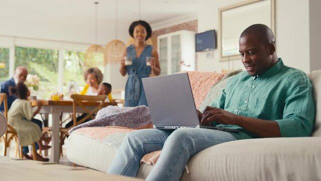 Parents indoors at home on sofa looking at laptop with grandparents and children in background - shot in slow motion