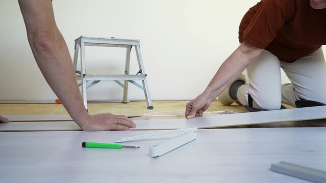 Mature married couple installing new wooden laminate flooring on a warm floor. Renovation, new life concept
