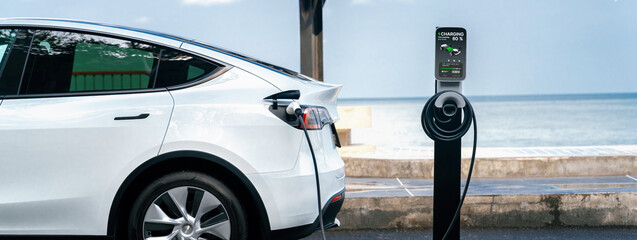 Electric car recharging battery at outdoor EV charging station for road trip or car traveling by...