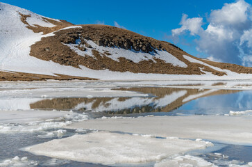 Fototapeta na wymiar Il lago di montagna semi ghiacciato a fine inverno e i riflessi