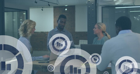 Image of graph icon in circles over diverse coworkers discussing reports in office
