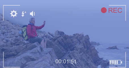 Smartphone image interface screen over caucasian senior man sitting on coast filming sea view
