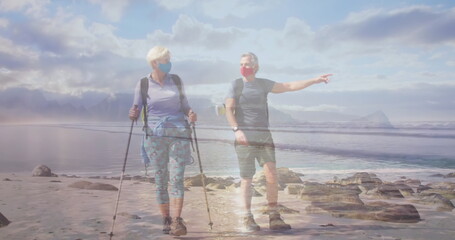 Caucasian senior couple in face masks hiking on the coast, over moving sea