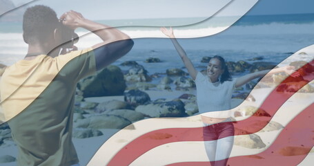 Image of american flag over african american couple taking photo at beach