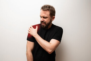 Shoulder pain problem concept: bearded man in black t-shirt holds his shoulder