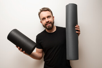 Wellness self care fitness concept: happy bearded hipster holds yoga mat and foam roll