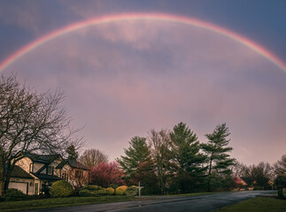 Midwestern suburban street in early spring after rain with  rainbow in the sky; deer at distance