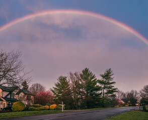 View of suburban Midwestern street in early spring after rain with  rainbow in the sky; several deer at distance