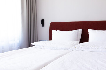 Clean Bedding sheets and pillow on natural wall room background. White bedding and pillow in hotel room. White pillows on empty bed.