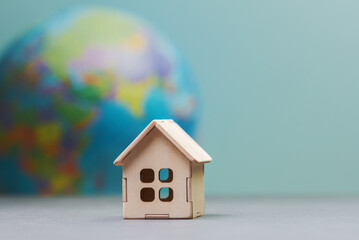 Craft wooden house model against blurred globe in the background suggests a context of global housing or real estate - 768253347