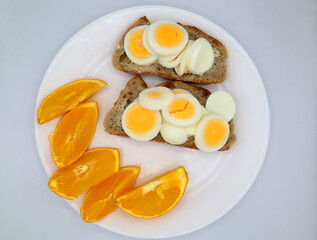 Egg sandwich and sliced oranges on a white plate.