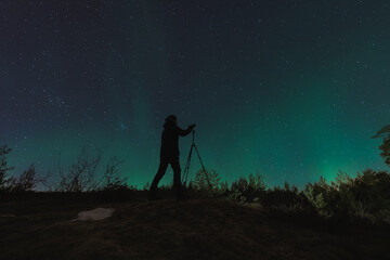 A landscape astro photographer with a camera on a tripod takes pictures of the starry sky and the...