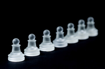opaque glass chess pawn row on black background, selective focus, closeup