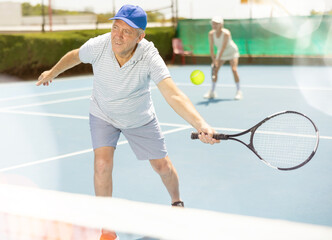 Senior man playing tennis on court holding tennis racket. Retirement retreat and active senior lifestyle concept.