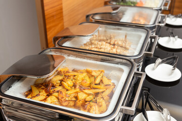 Fried potatoes garnish and meat on skewers in a food warmer on a buffet table in a hotel restaurant.