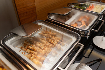 Fried meat on skewers and other appetizers in a food warmer on a buffet table in a hotel restaurant.