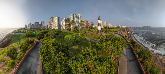 Image of the Miraflores lighthouse in Lima, Peru. Surrounded by vegetation, buildings and the sea with sunset light.
